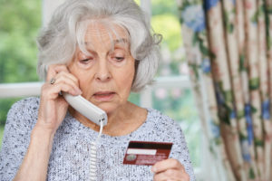 Concerned senior woman on phone looking at credit card