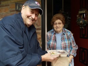 Man meeting woman at door with Meals on Wheels delivery