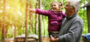 Older, white-haired man holding his happy, toddler daughter on an autumn day in the woodds
