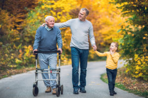 Elderly father using walker and adult son and grandson out for a walk in the park. in the fall
