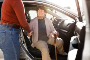 A caregiver helping an older women out of her car.