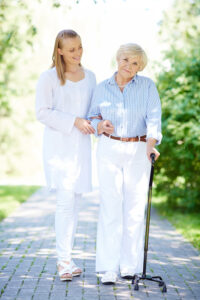 An older women and her daughter on a walk outside. The older women is using a cane.