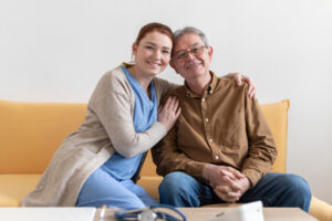 An older adult and his caregiver smiling on the couch.