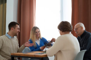 A family playing bingo at the dining room table. An older couple, on the right, and their grownup kids on the left.