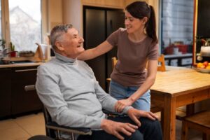 An older man in a wheel chair and his daughter are laughing in the kitchen.