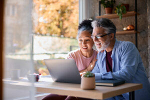 Surprised senior couple sitting together at home, gazing at their laptop screen, sharing in the joy of good news and experiencing a moment of happiness and connection