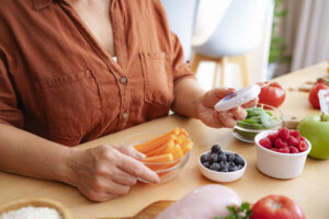 Unrecognizable woman reading blood glucose level results using a glucometer. Healthy food ingredients recommended for diabetic patients are on the table